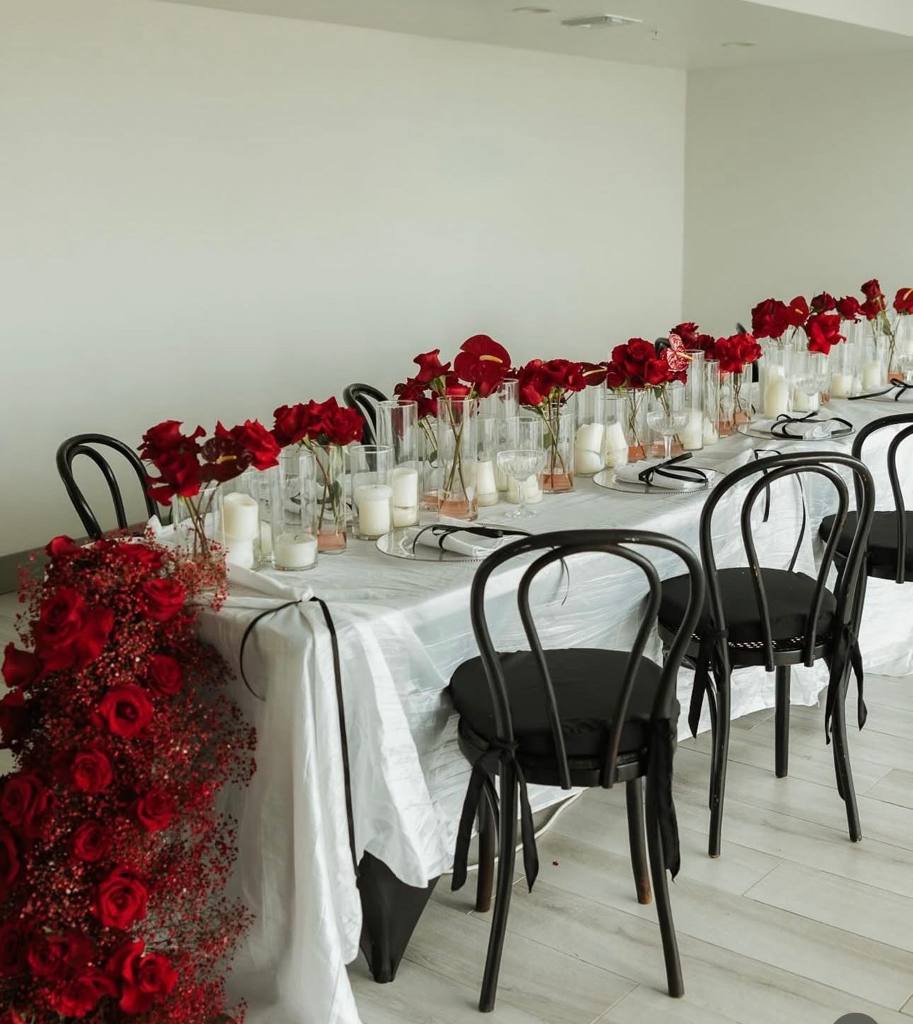 Long table set for a formal event, decorated with red roses and candles. Black chairs surround it.