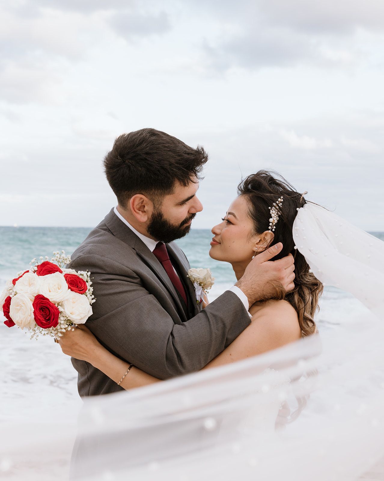 A bride and groom are kissing on the beach.