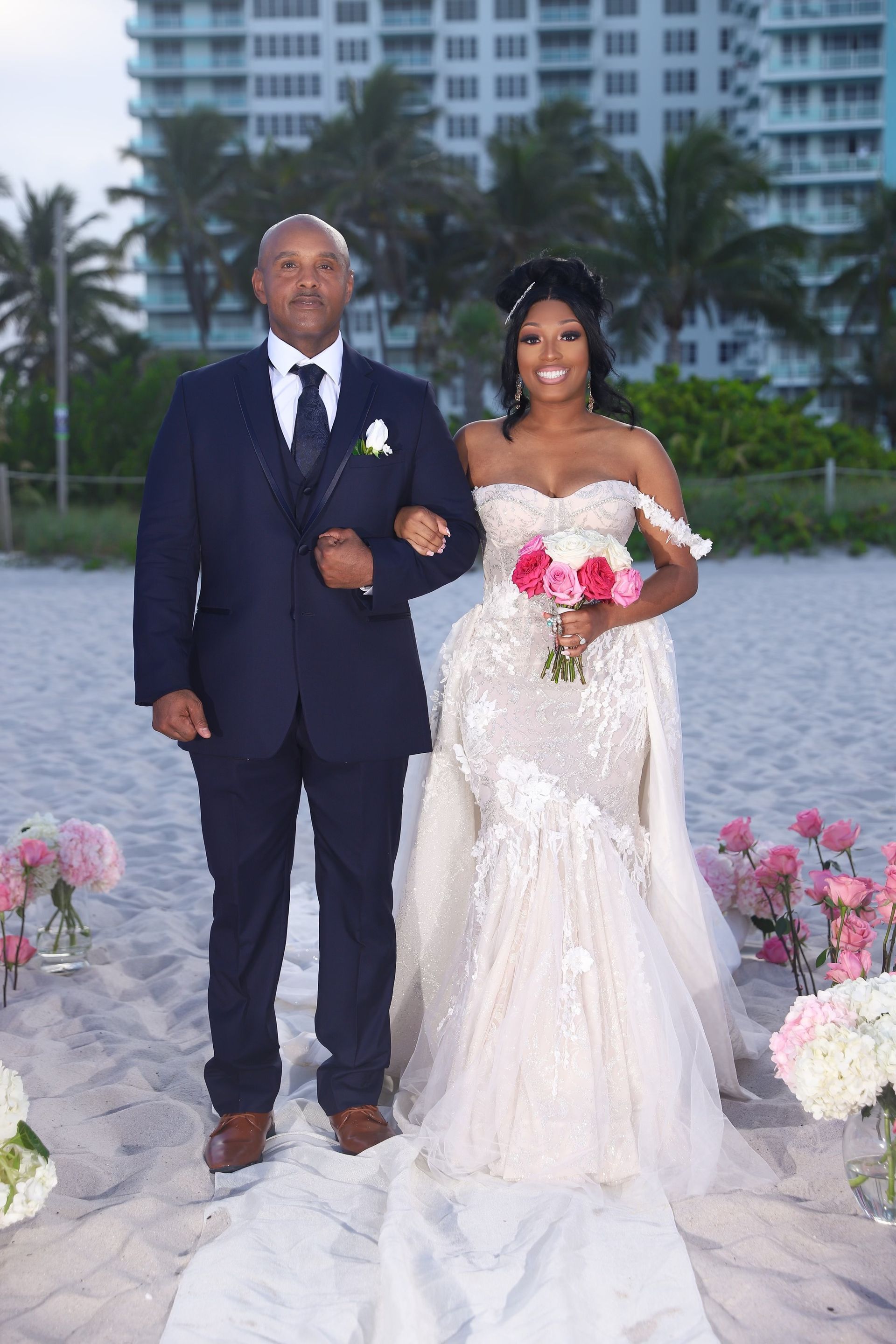 A bride is walking down the aisle with her father on the beach.