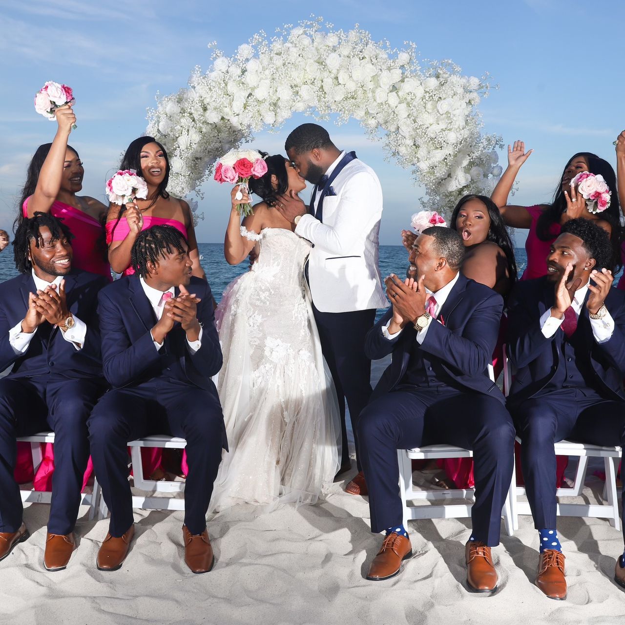 A bride and groom are kissing in front of their wedding party