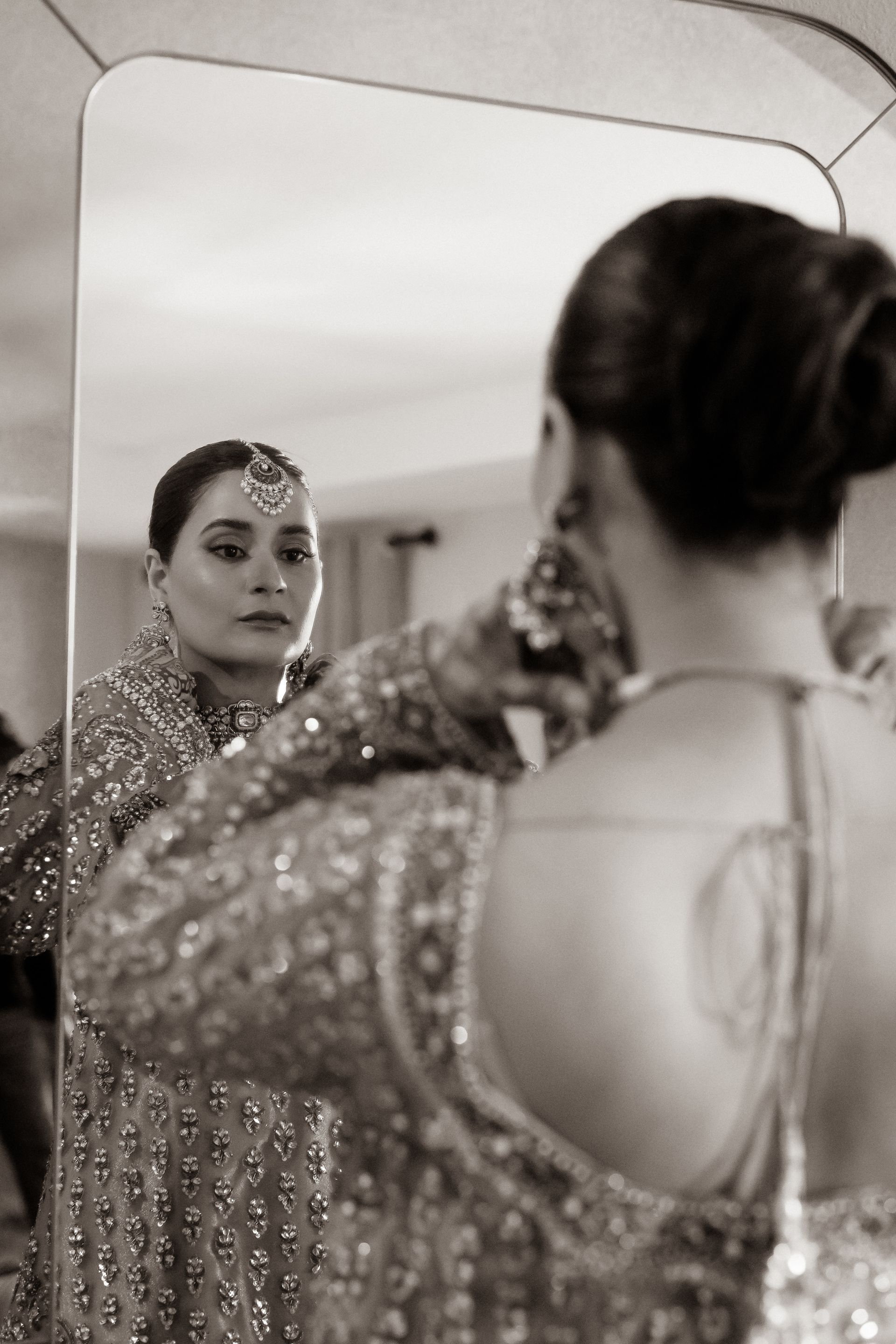 Woman in ornate dress and jewelry, looking in mirror.