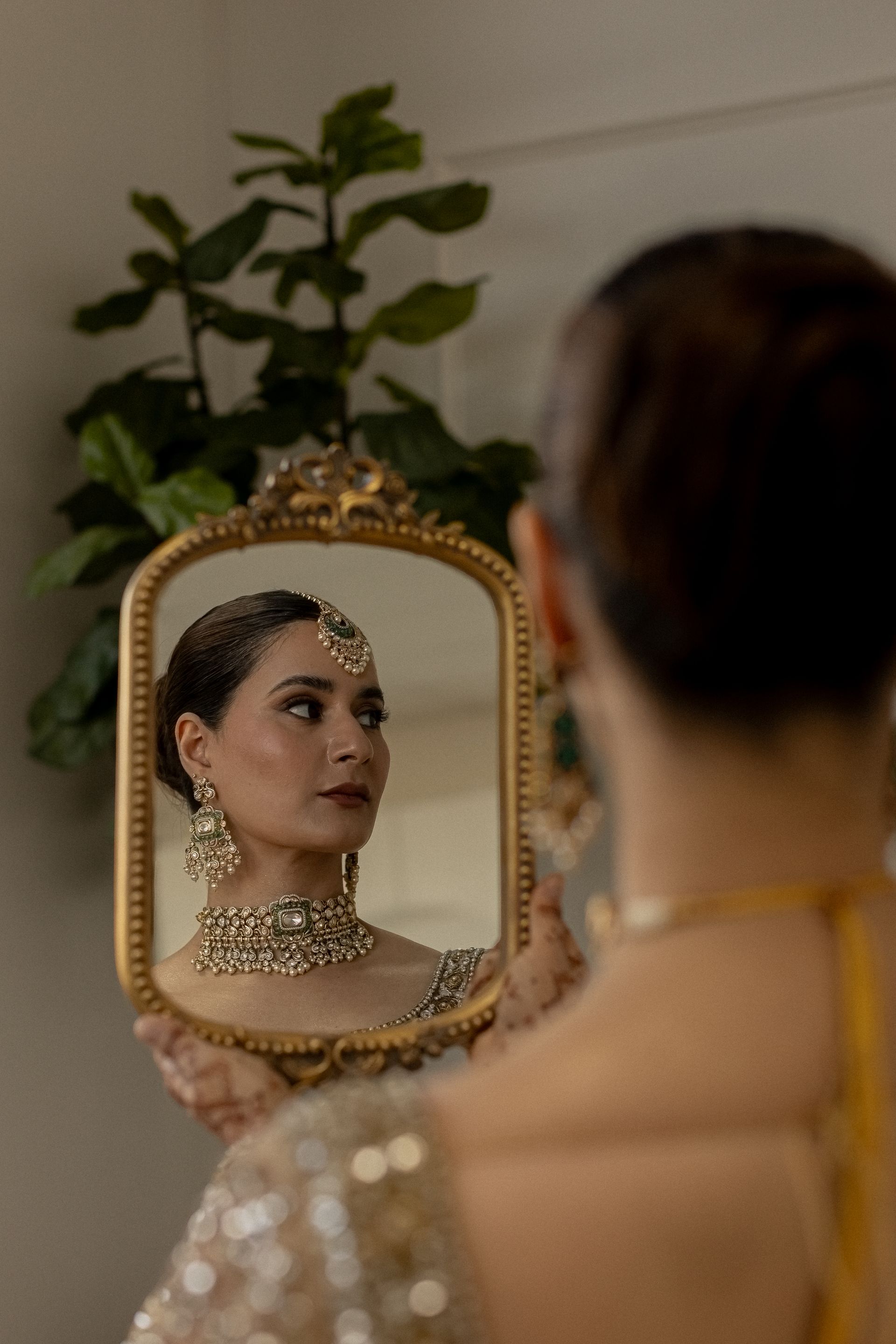 Woman looking at herself in a mirror, wearing jewelry and holding the frame.