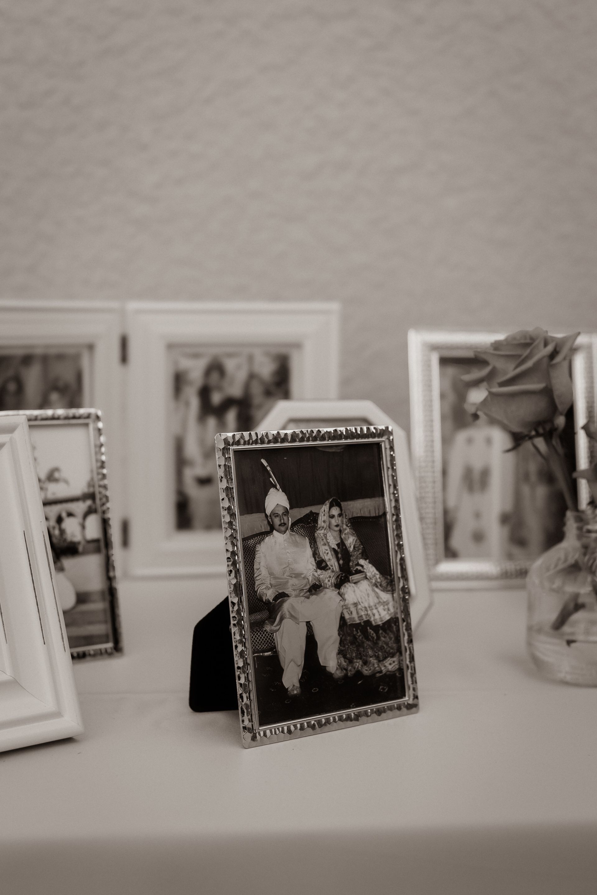 Framed vintage photograph of a couple; surrounded by other framed photos and a vase with a rose.