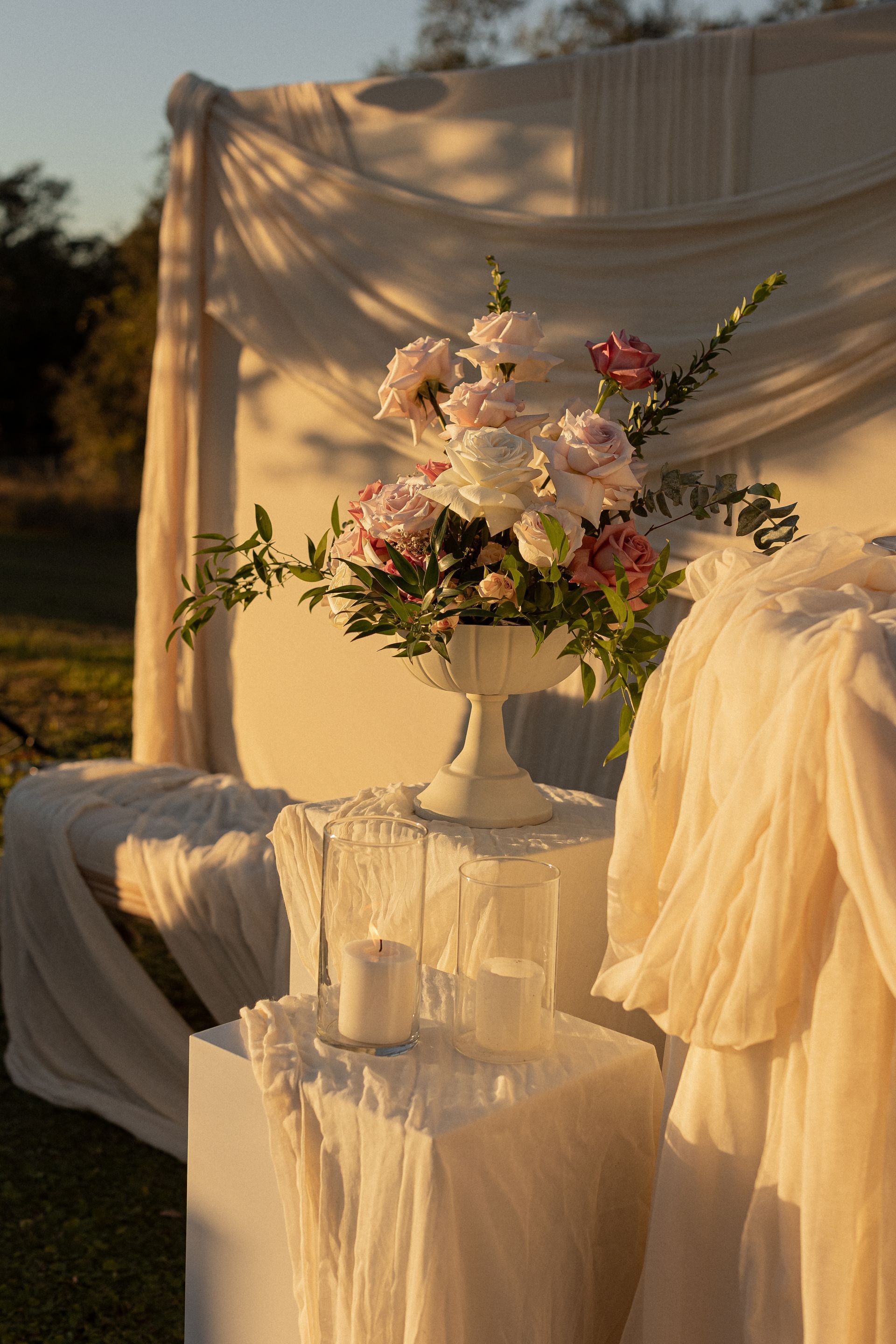 White floral arrangement and candles on a draped table, set outdoors with soft light.