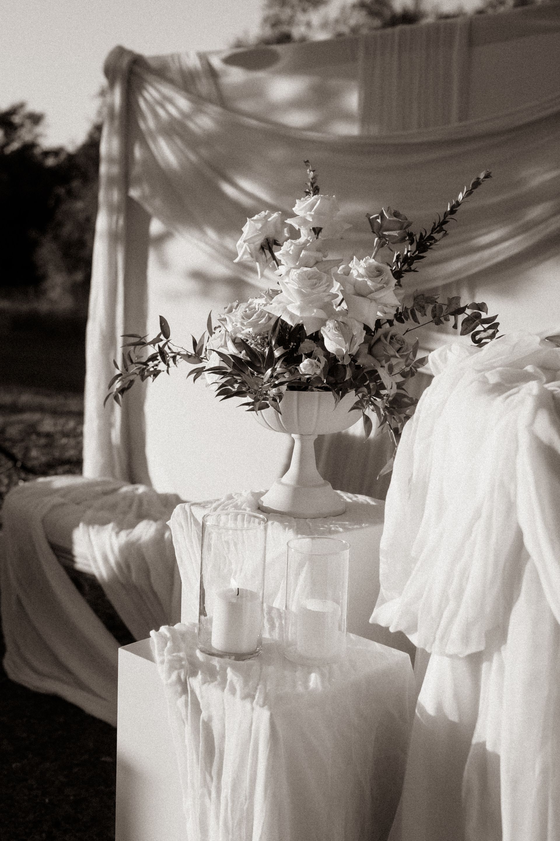 White floral arrangement on a pedestal with draping fabric, lit candles, and sheer backdrop in Orlando Luxury backyard wedding
