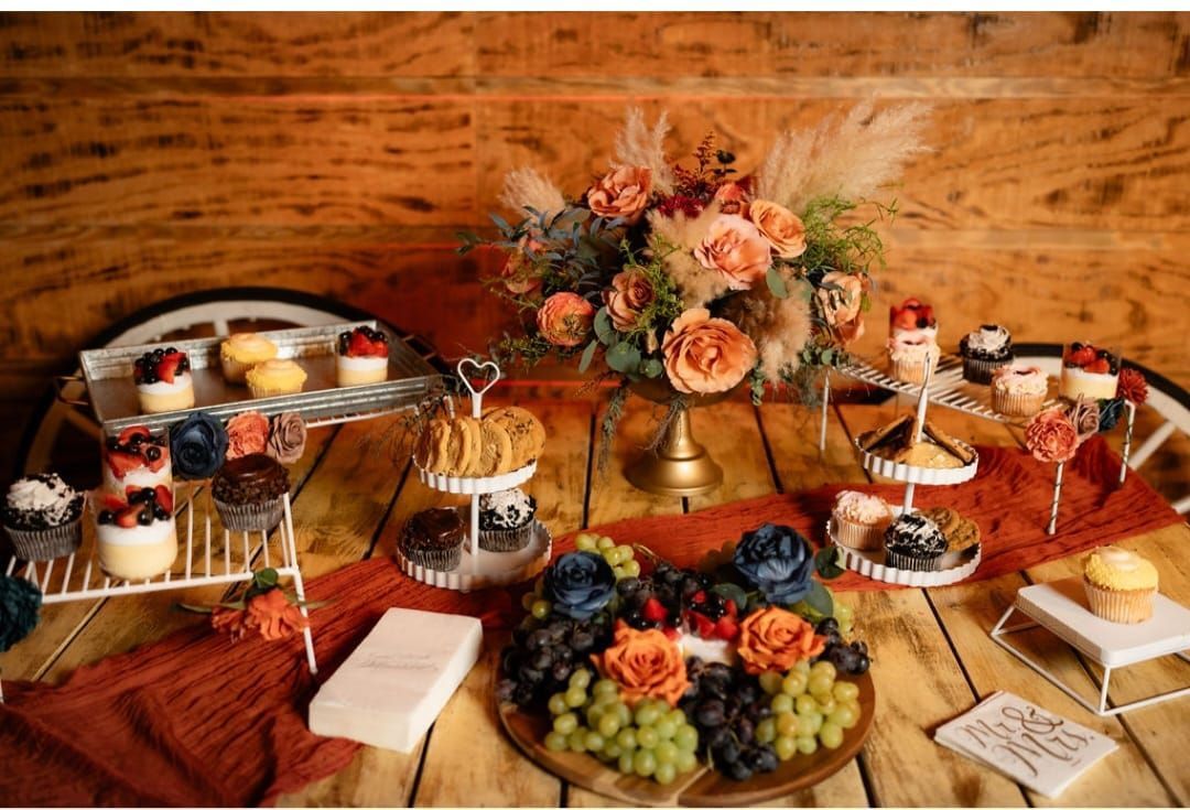 A wooden table topped with a variety of desserts and flowers.