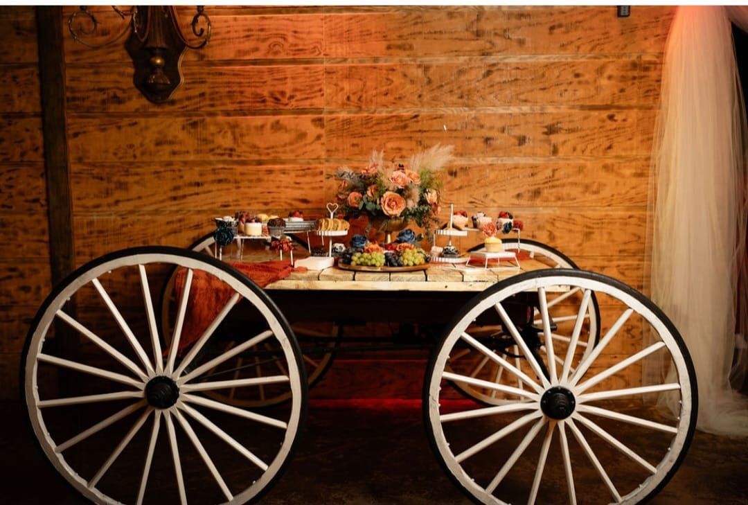 A horse drawn carriage with white wheels is sitting in front of a wooden wall.