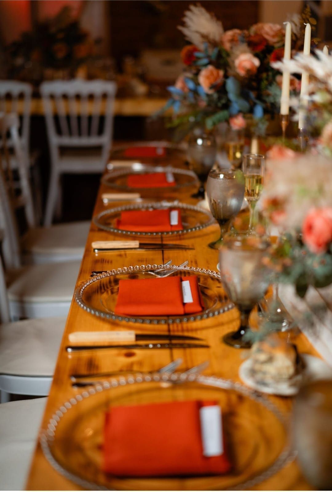 A long wooden table with plates , napkins , utensils and flowers on it.