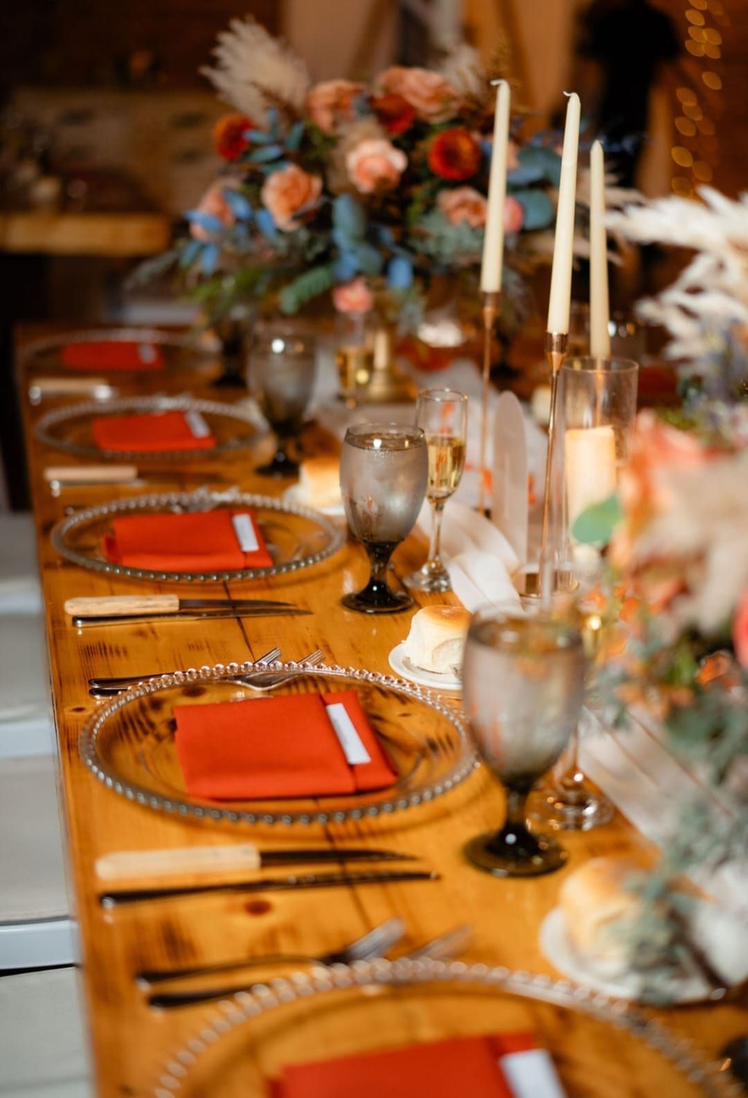 A long wooden table set for a wedding reception with plates , glasses , candles and napkins.
