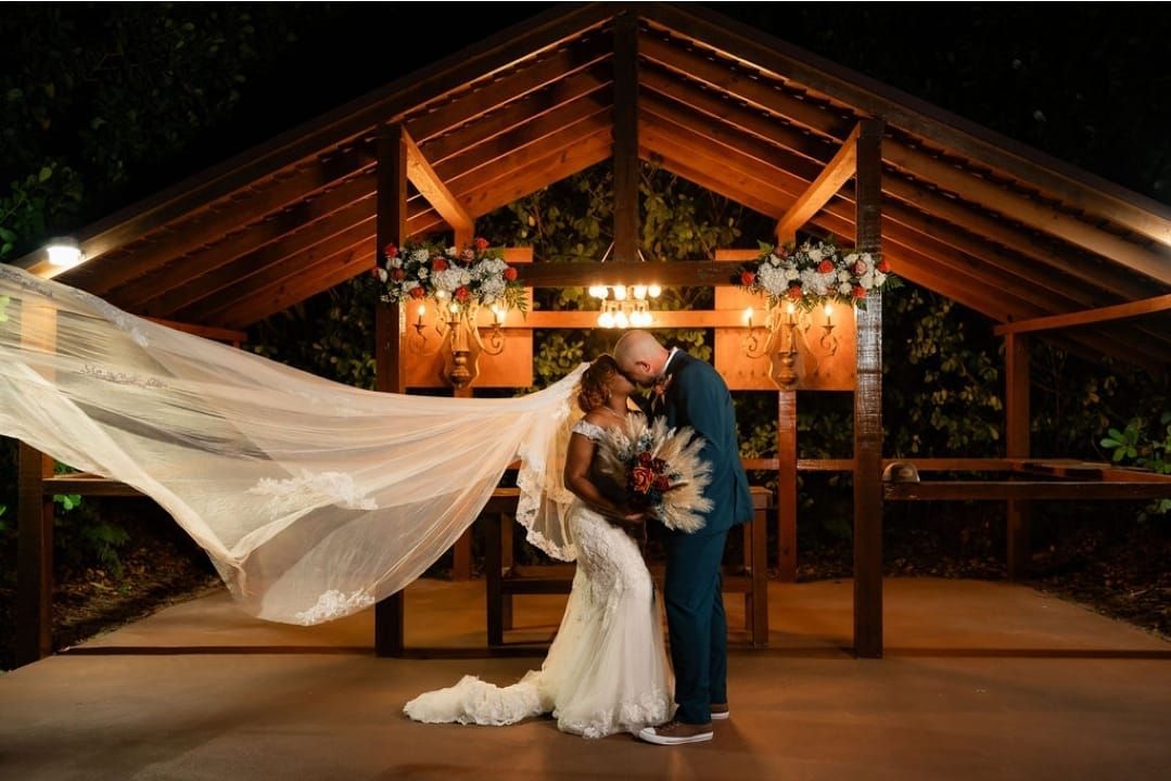 A bride and groom are kissing under a gazebo at their wedding.