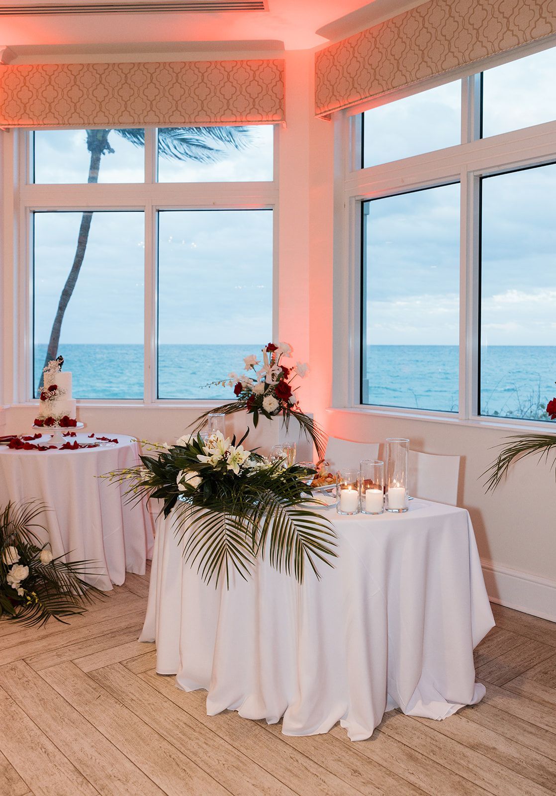 A table with flowers and candles on it in front of a window overlooking the ocean.