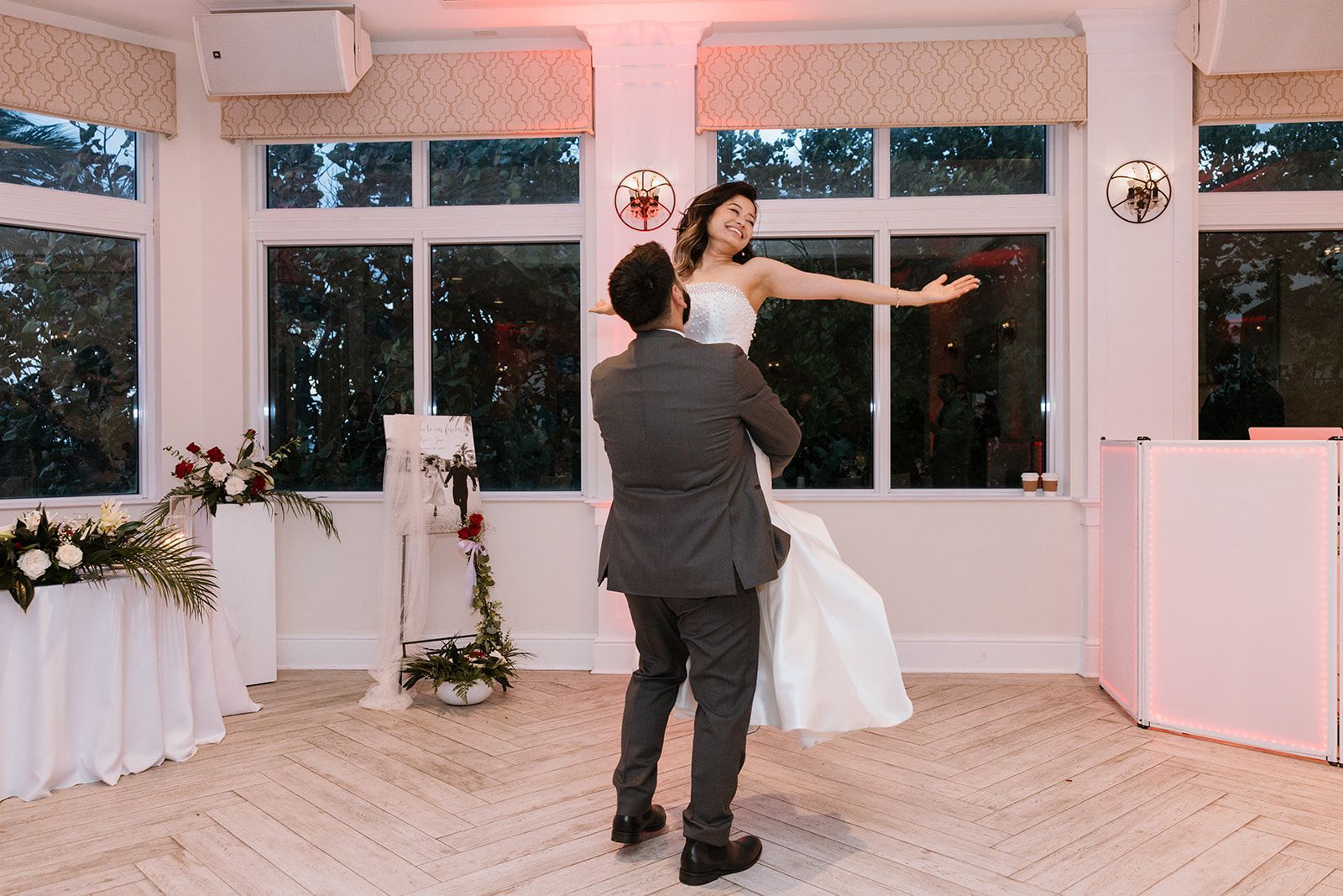 A bride and groom are dancing in a room with lots of windows.
