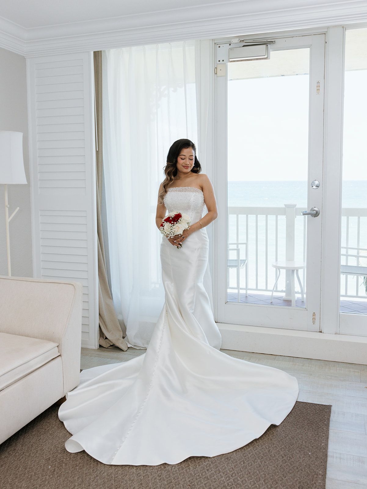 A bride in a wedding dress is standing in front of a window holding a bouquet of flowers.