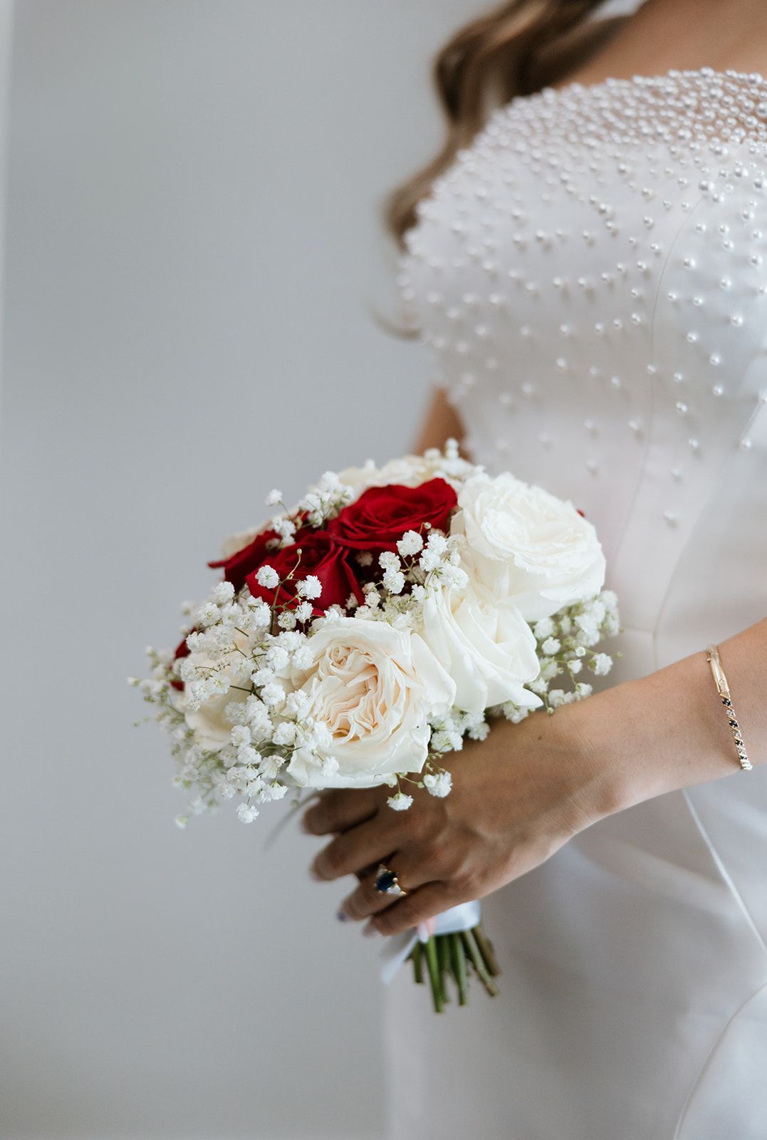 A bride in a white dress is holding a bouquet of red and white flowers.