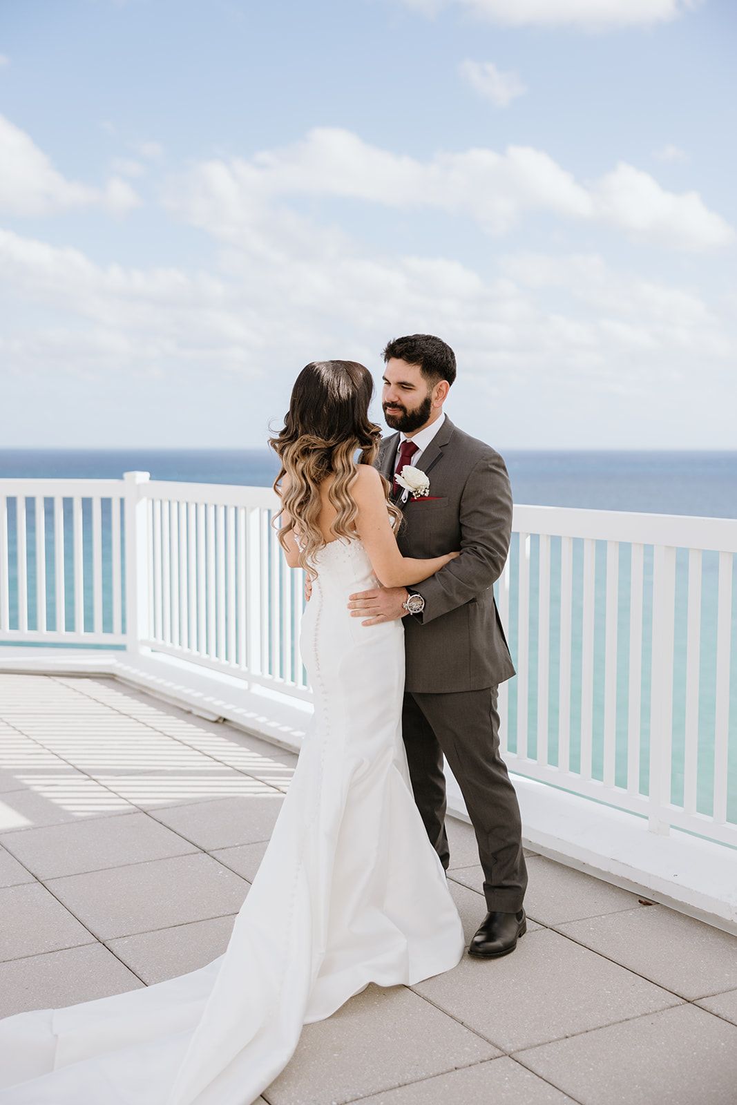 A bride and groom are standing next to each other on a balcony overlooking the ocean.