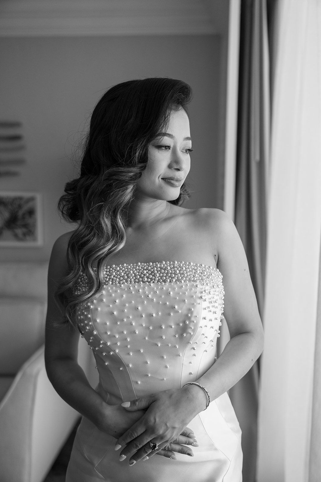 A woman in a wedding dress is standing in front of a window.