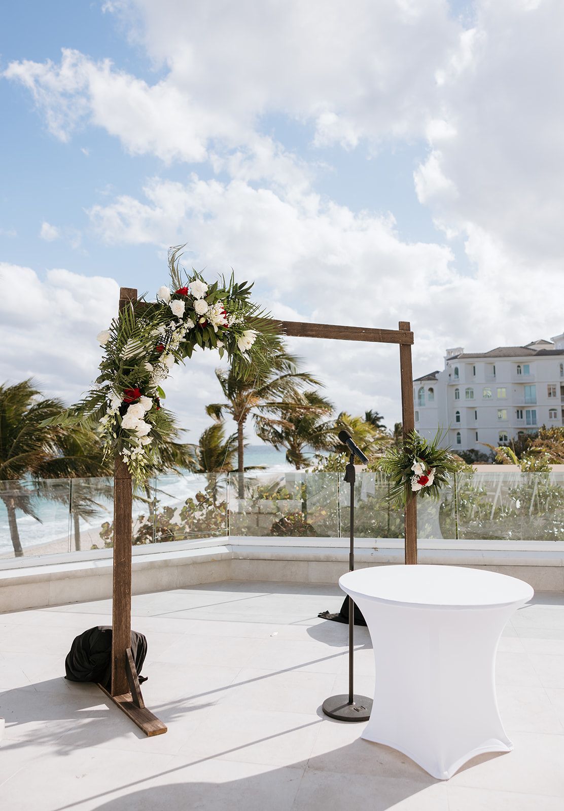 A wooden arch decorated with flowers is sitting next to a table on a balcony.