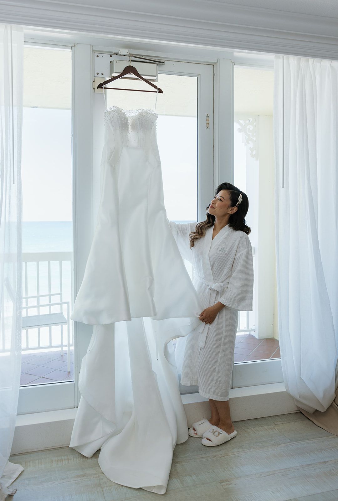 A woman is standing in front of a window holding a wedding dress.