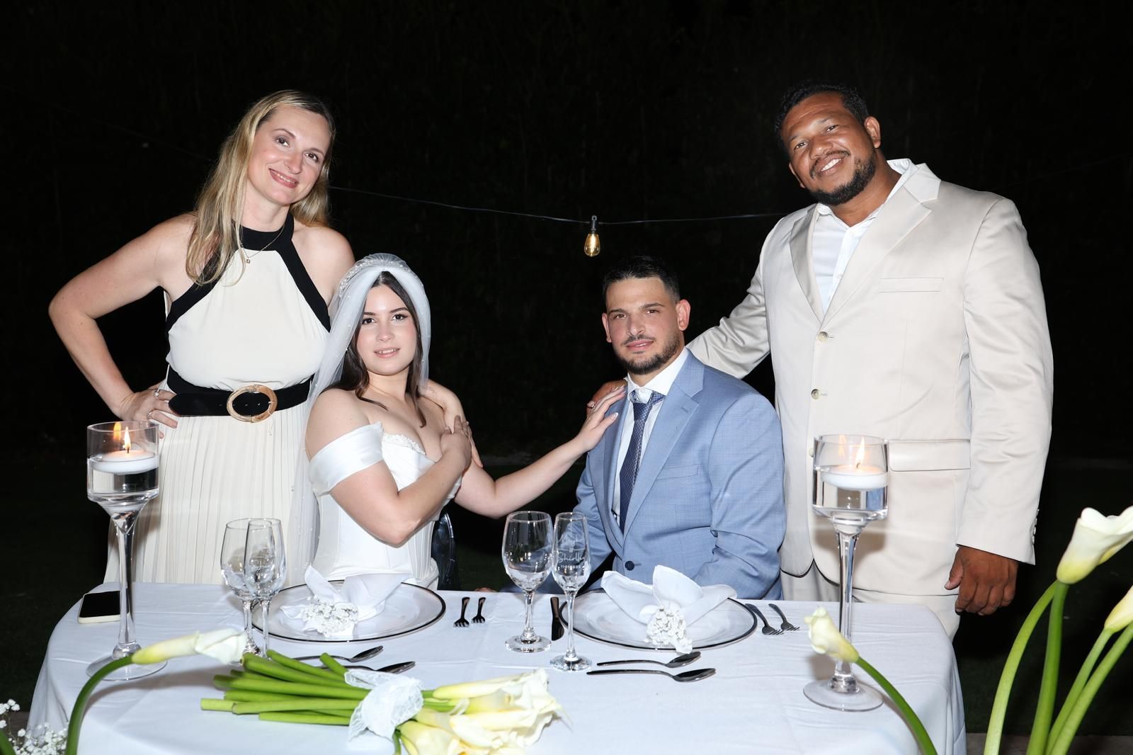 Couple at wedding table with two guests, nighttime outdoor setting.