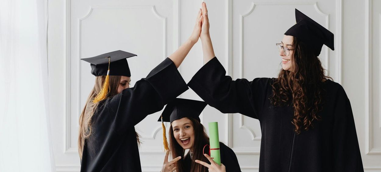 Three graduates in caps and gowns celebrate with high fives.