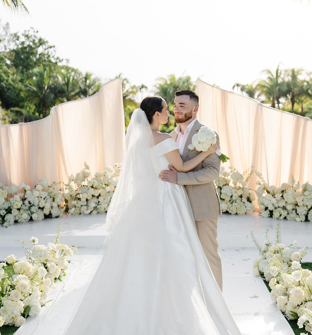 Custom wedding arch - wave shape with drapes, ivory and cream color florals around the altar and ceremony aisle  while bride and groom kissing