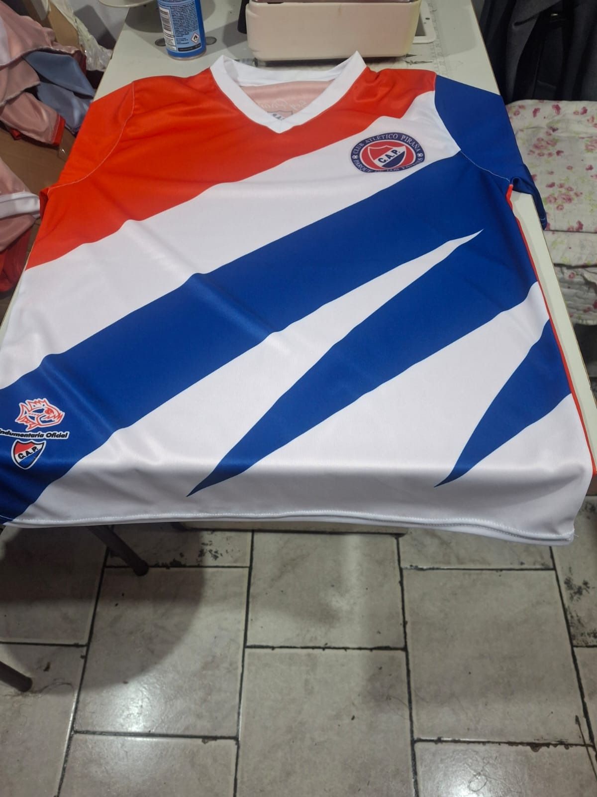Camiseta de fútbol con rayas diagonales rojas, blancas y azules, y el logotipo del equipo en el pecho y la manga.