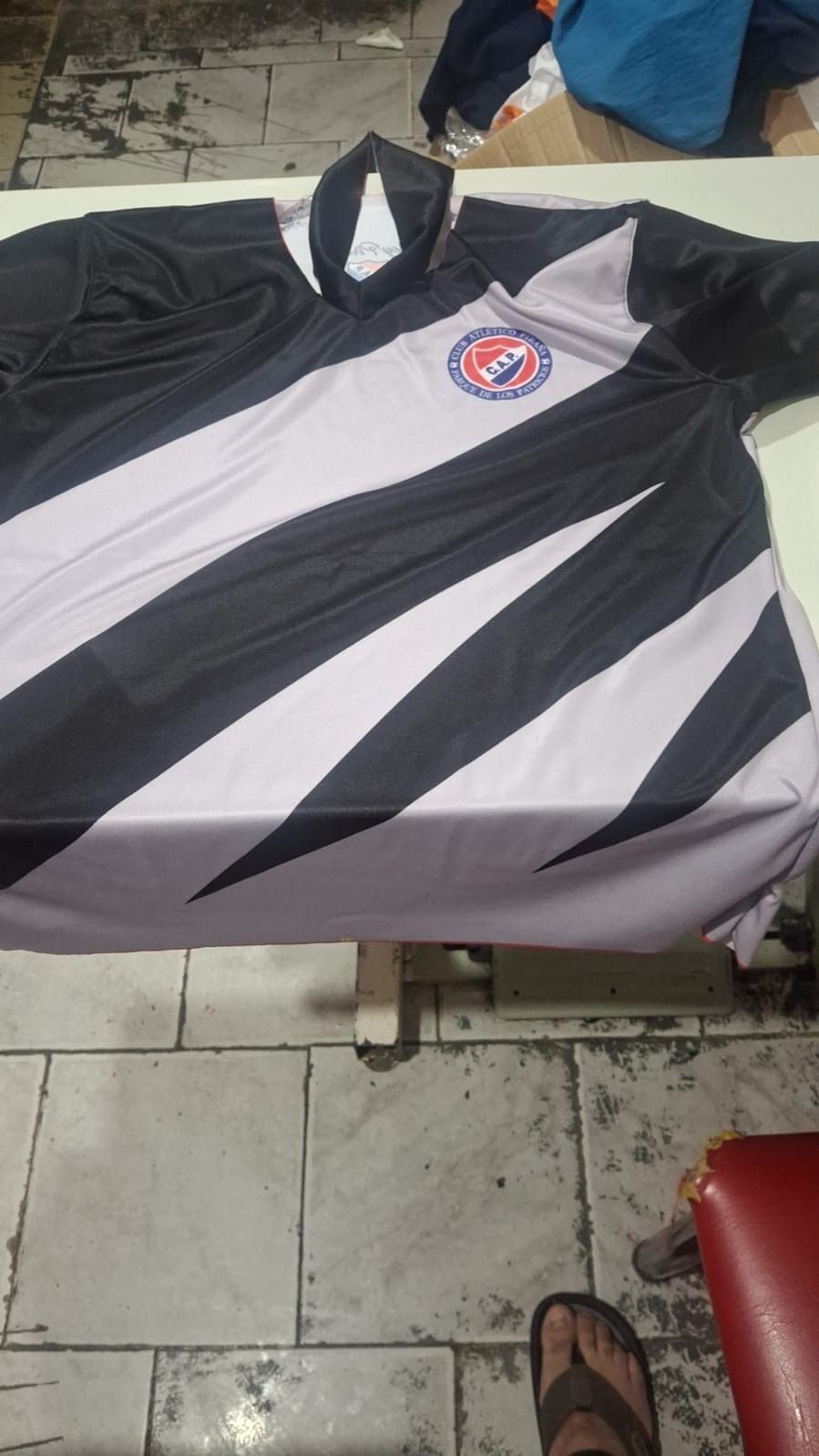 Camiseta de rayas blancas y negras con logotipo, colocada sobre una mesa.