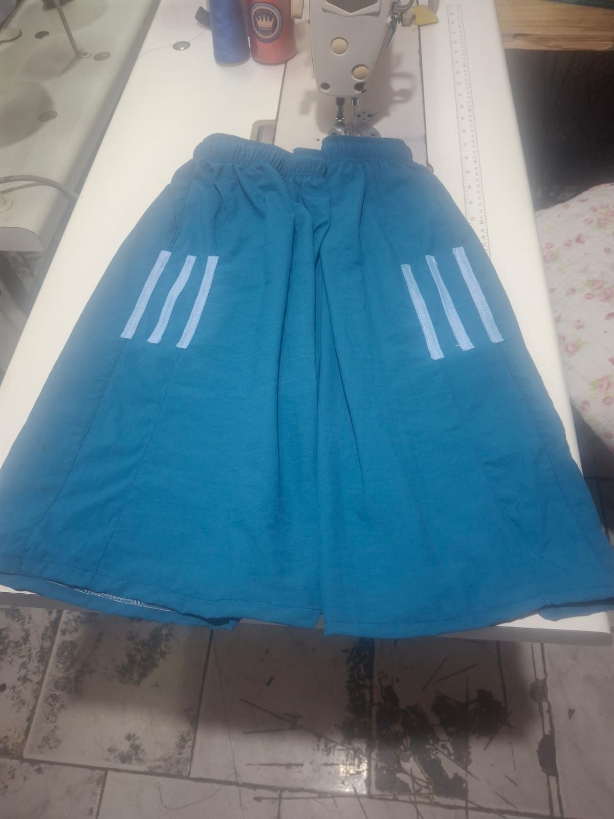 Pantalón corto deportivo de color azul con tres rayas blancas en los laterales, sobre una superficie blanca.