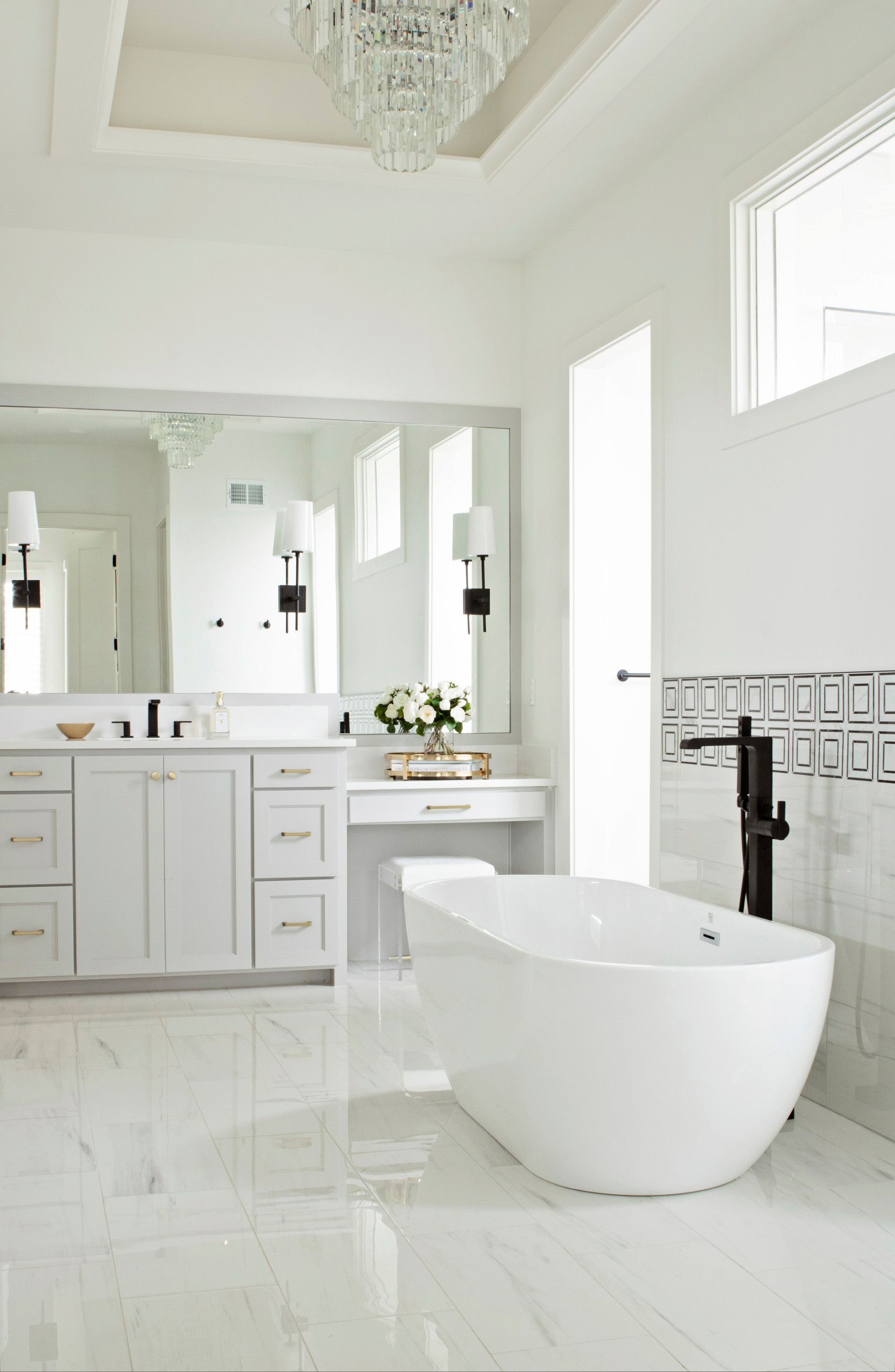 A bathroom with a tub , sink , mirror and chandelier.