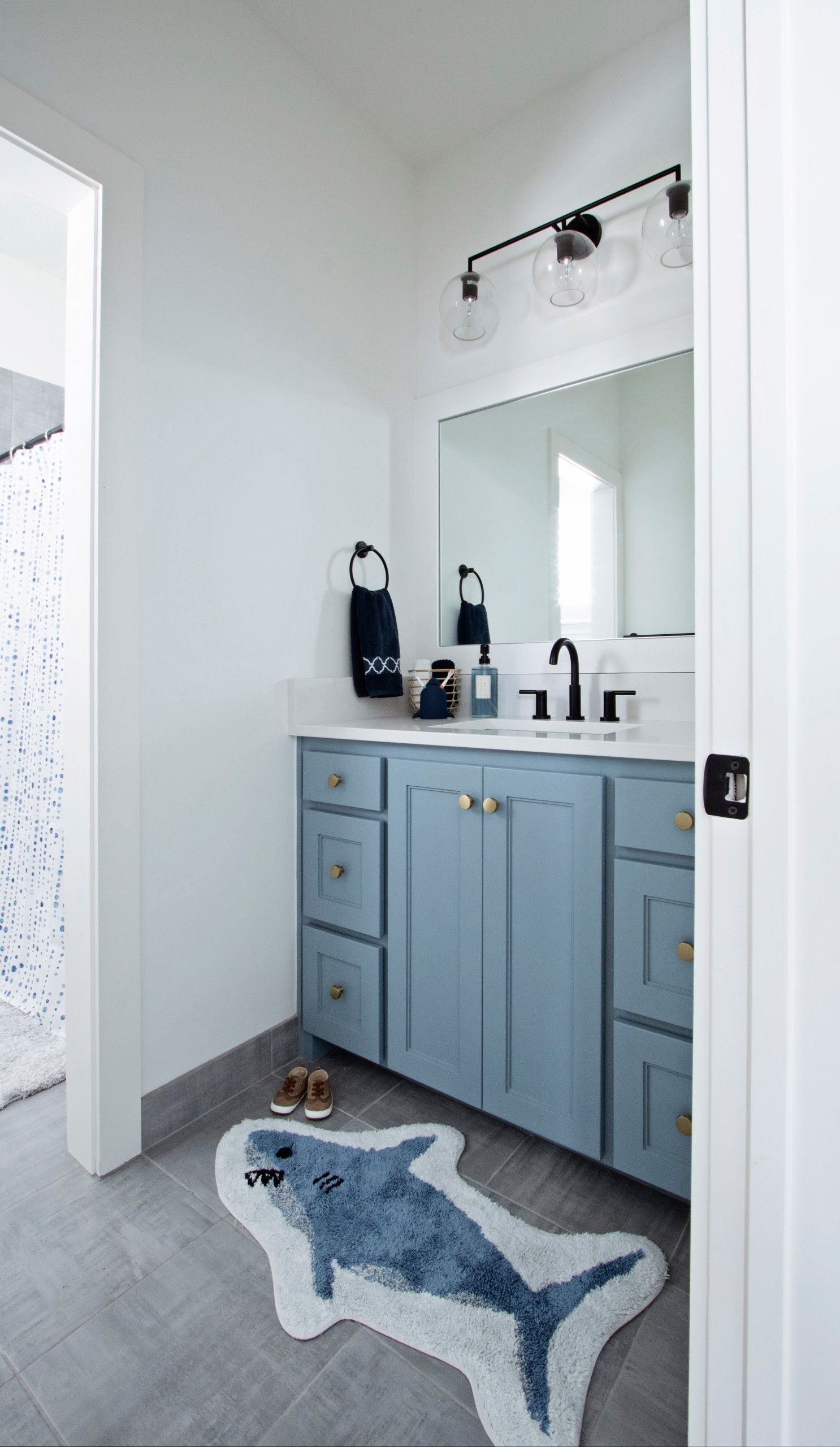 A bathroom with a sink , mirror , and rug in the shape of a shark.