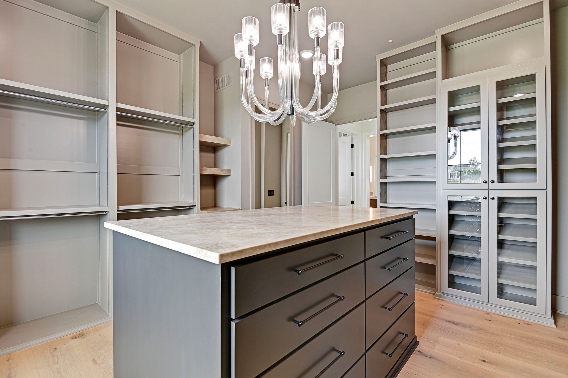 A walk in closet with a large island in the middle and a chandelier hanging from the ceiling.