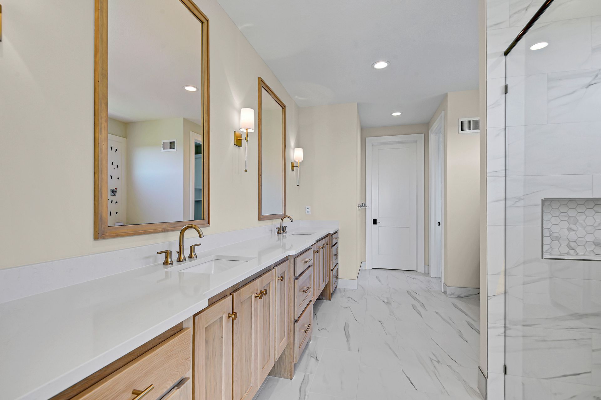 A bathroom with two sinks , two mirrors and a walk in shower.