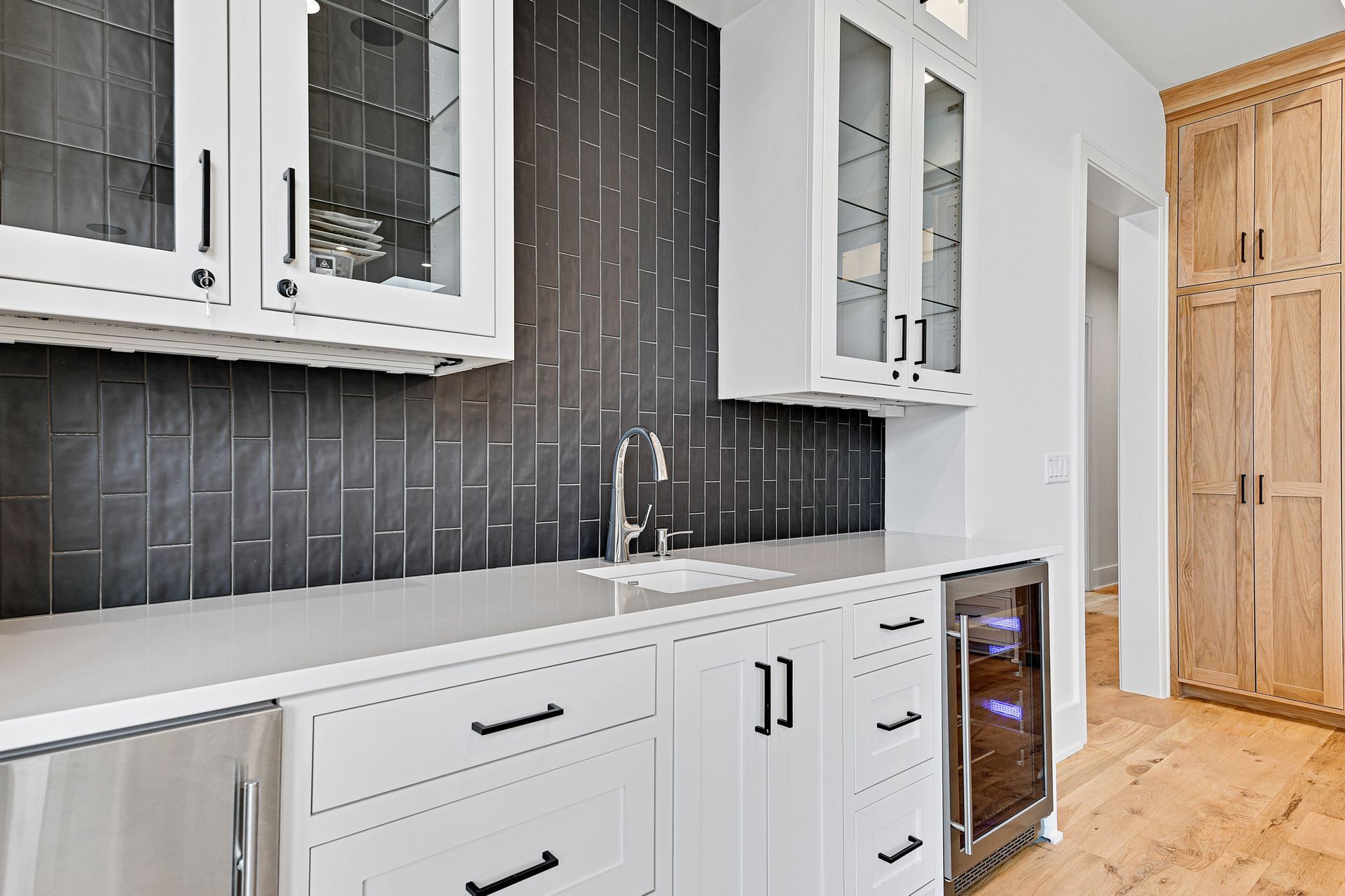 A kitchen with white cabinets , stainless steel appliances , a sink , and a wine cooler.