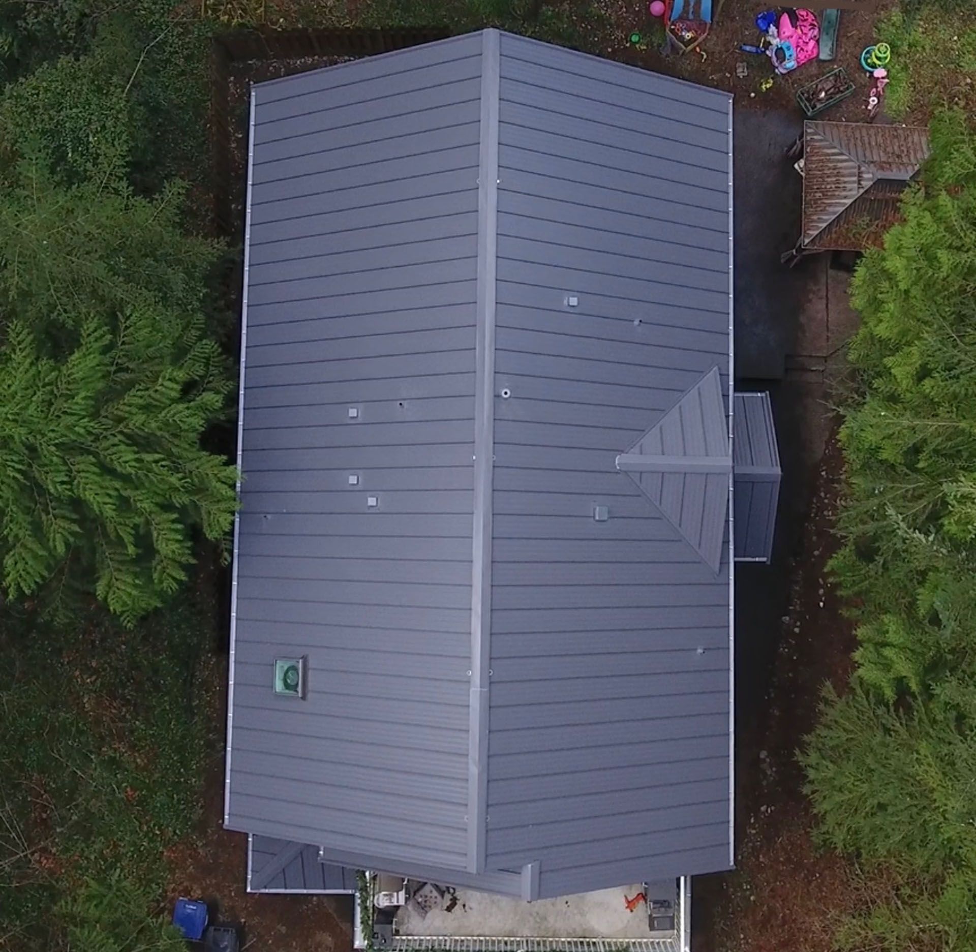 Aerial view of a gray-roofed house surrounded by dense green trees.