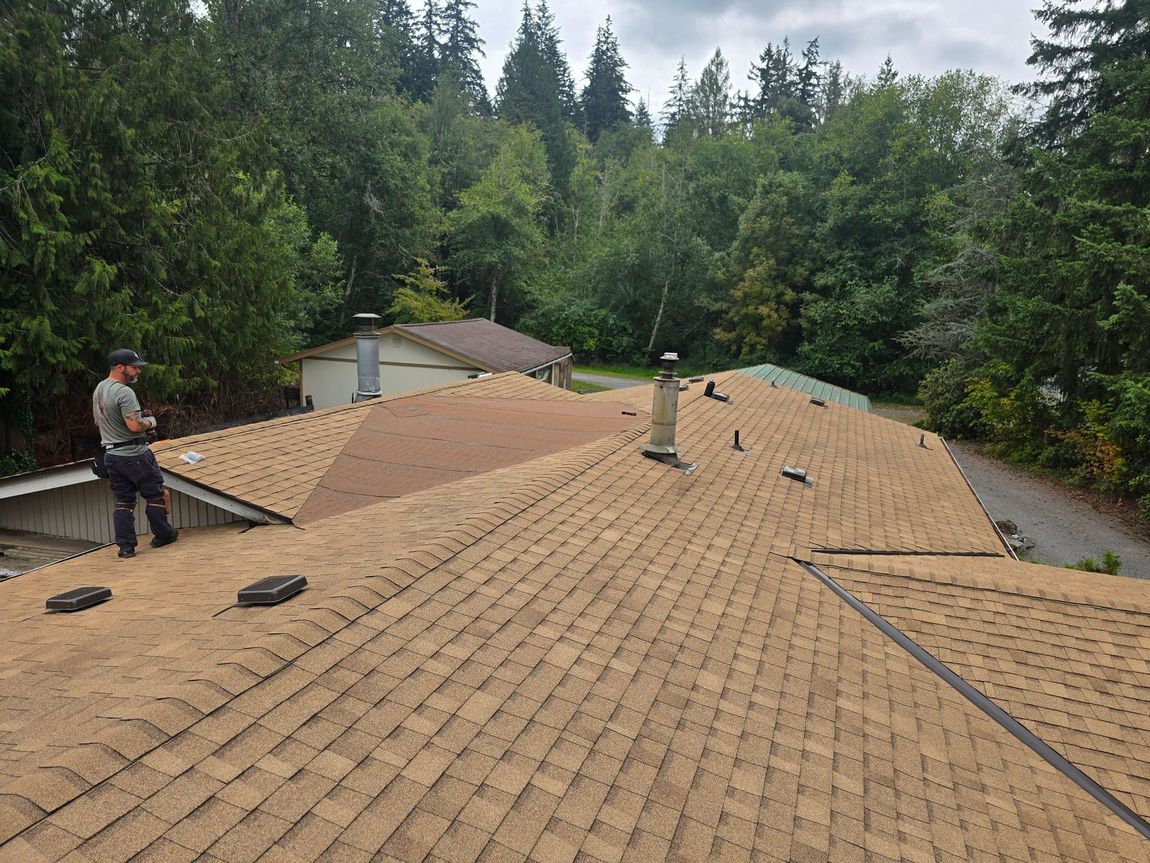 Canyon Roofing Northwest workerinstalling brown shingles on a roof in a wooded residential area