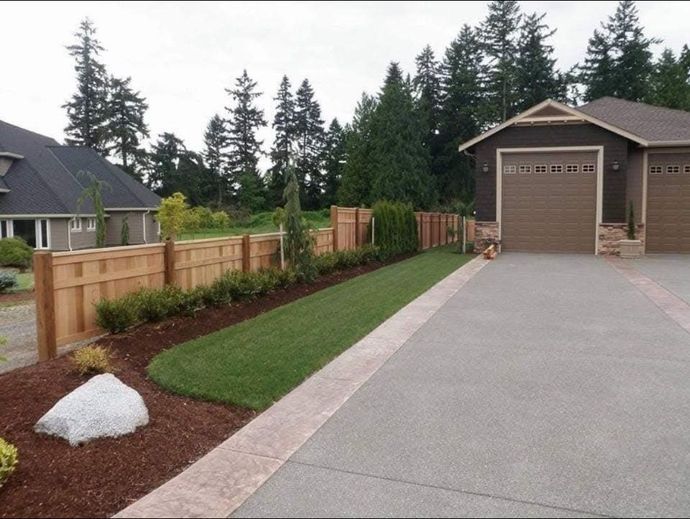 Residential driveway beside a landscaped lawn, wooden fence, and detached garage on a cloudy day