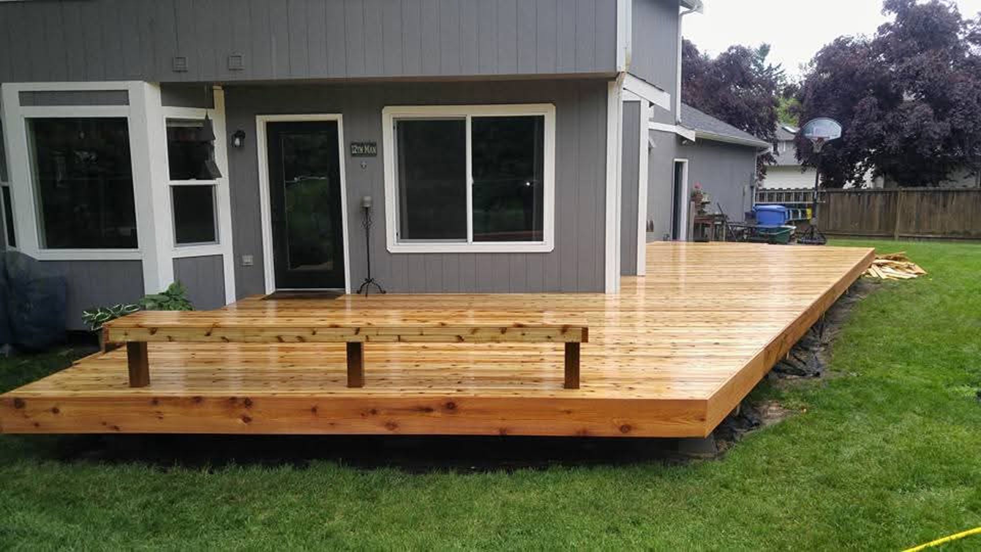 Wooden backyard deck attached to a gray house, with railings and a grassy yard