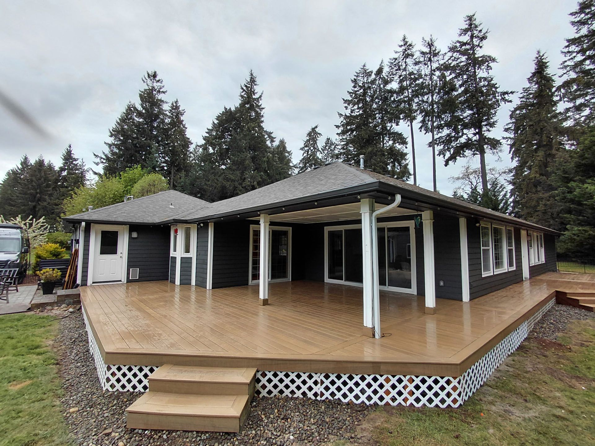 Single-story house with a covered wraparound porch and wooden deck surrounded by tall trees