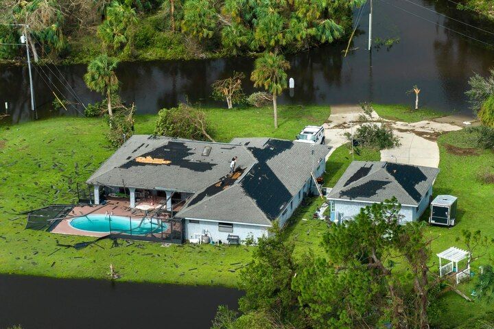 Aerial view of a house with a pool beside a canal, surrounded by trees and lawn