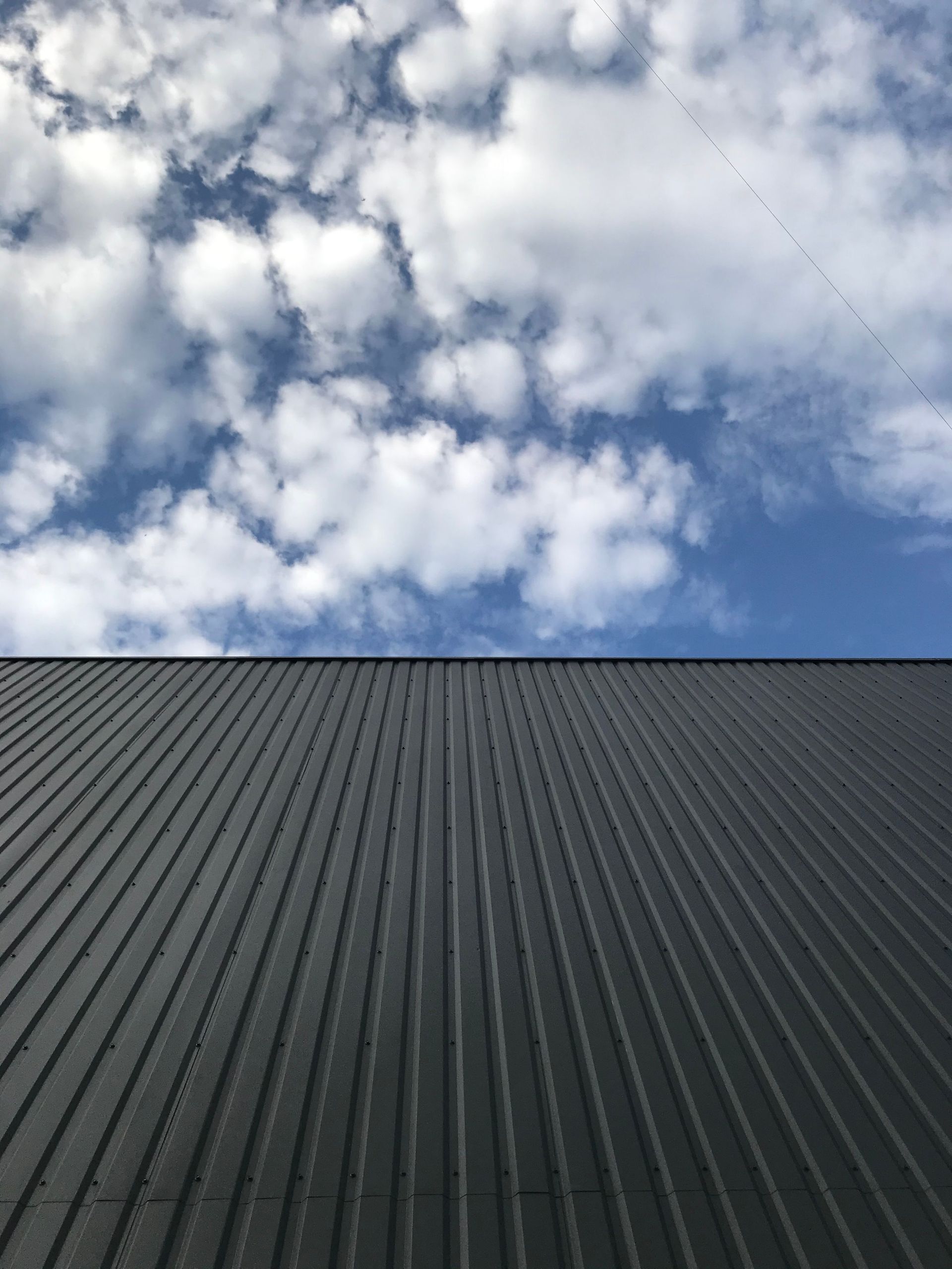 Dark corrugated roof beneath a cloudy blue sky