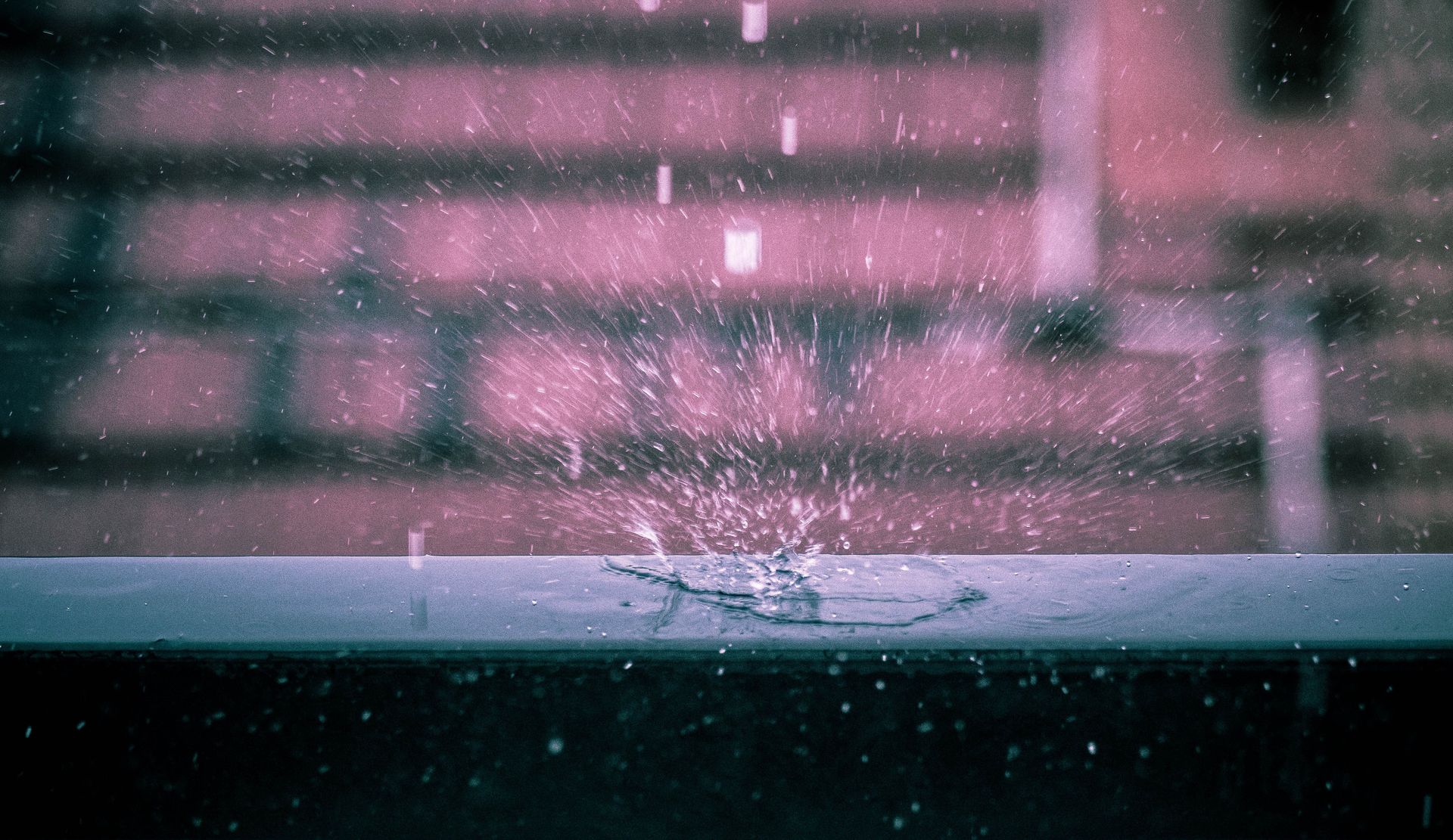 Pink-lit rainy window with water droplets and blurred city lights beyond a sill