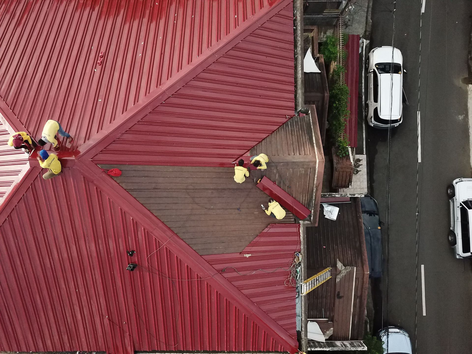 Workers repairing a red roof beside a street with parked cars