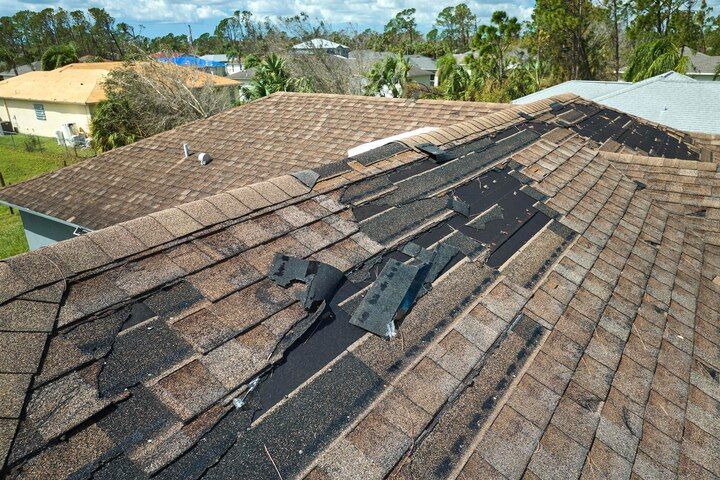 Damaged shingle roof with a long tear and exposed underlayment in a suburban neighborhood