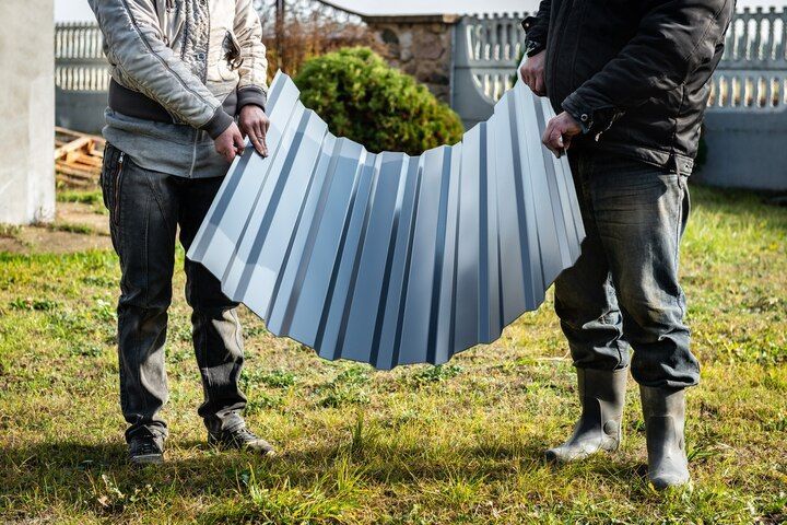 Two people holding a curved corrugated metal sheet outdoors on grass