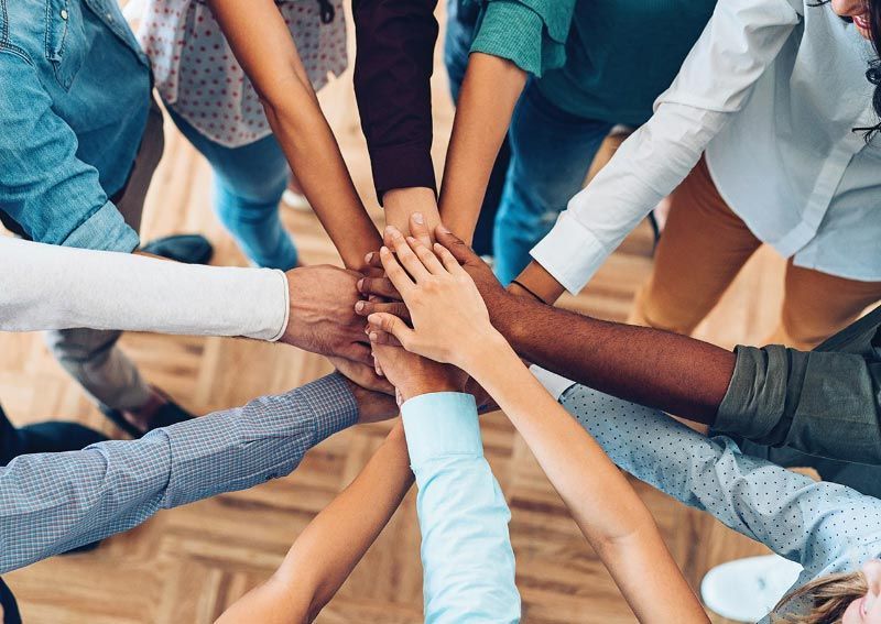 Hands of various skin tones in a circle, stacked in a team huddle.