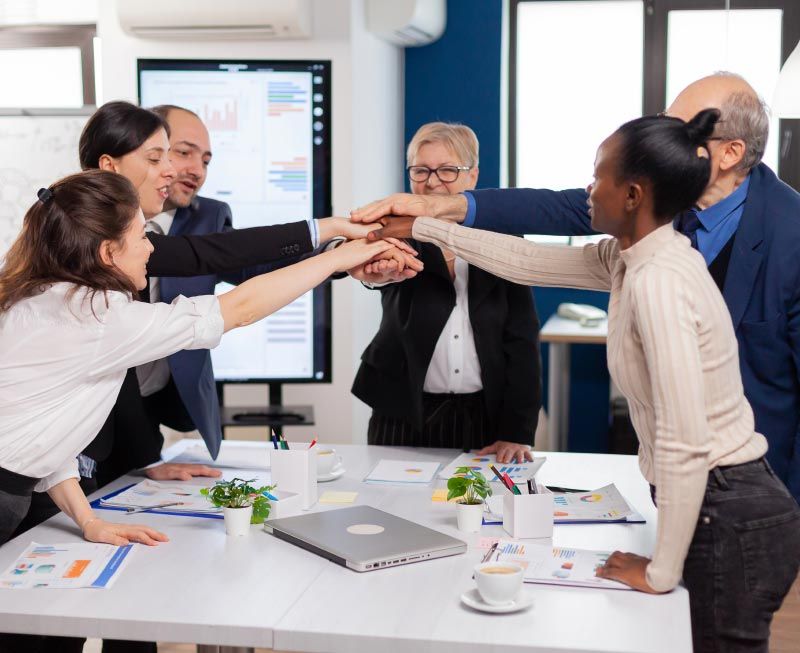Team of people with hands stacked together in office, symbolizing teamwork and collaboration.