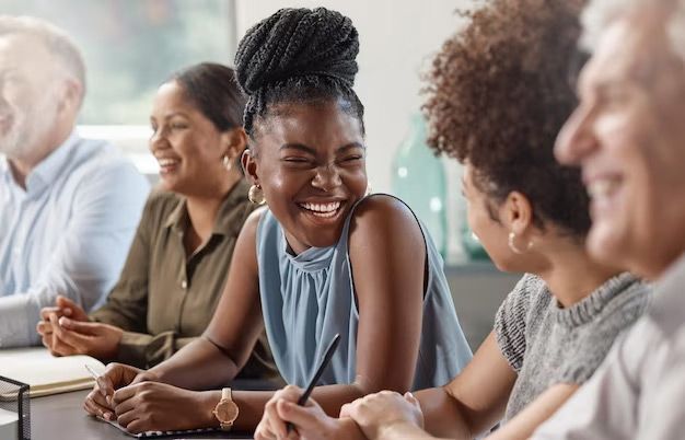 People laughing around a table. A woman with braided hair smiles widely.