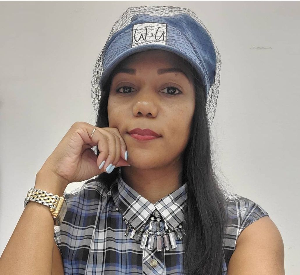 Woman wearing denim hat and plaid shirt, resting chin on hand.