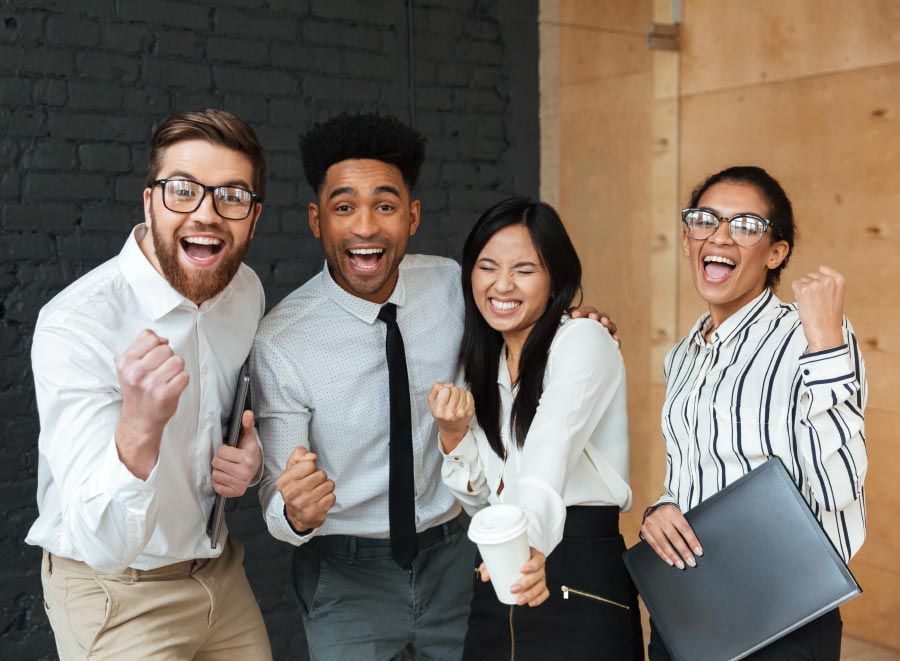 Four people in business attire celebrate with raised fists and joyful expressions.