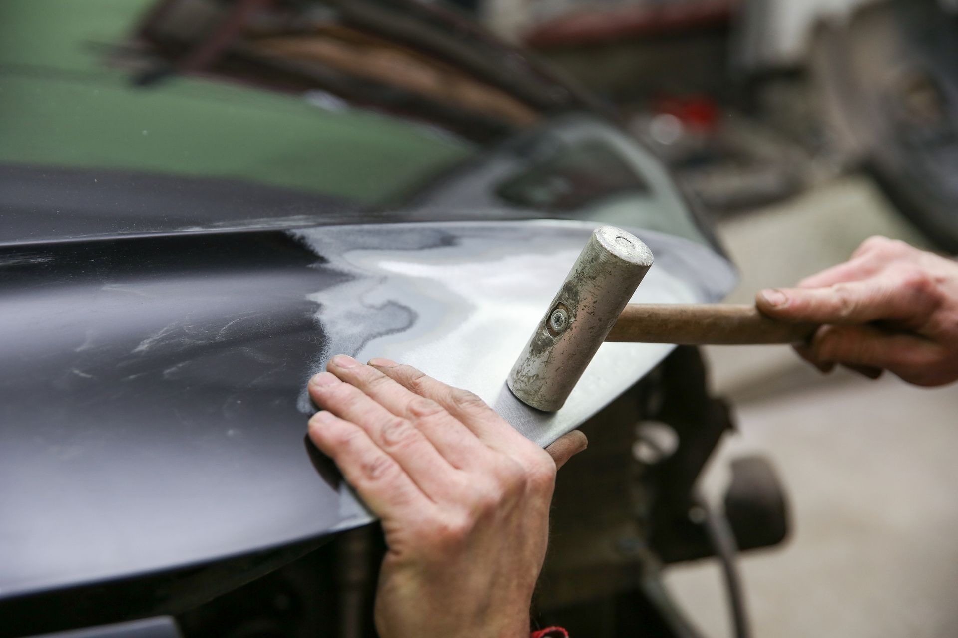 A person is using a hammer to fix a car hood.